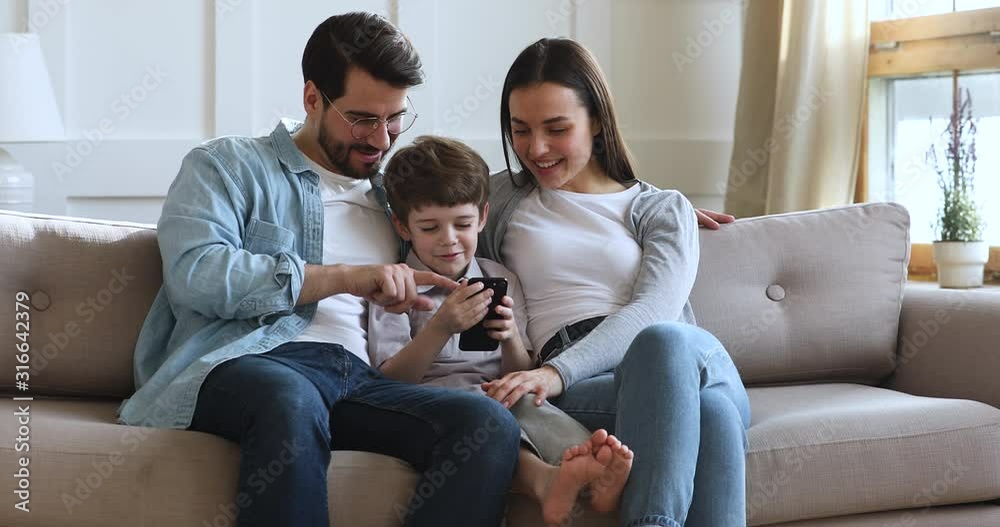 Smiling parents with kid son relax on sofa using smartphone Smiling parents with kid son relax on sofa using smartphone
