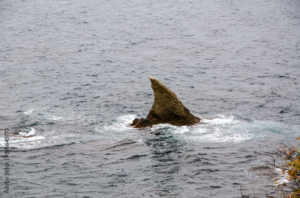Fototapeta premium Sharp rock protruding in the form of a shark fin above the surface of the sea.
