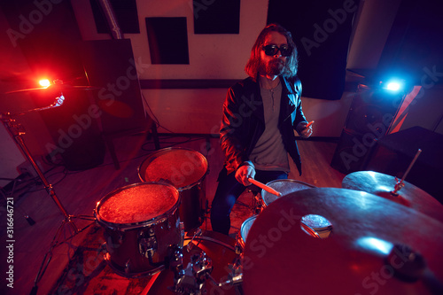 High angle portrait of handsome young man rocking drums during music concert in dim red lights, copy space