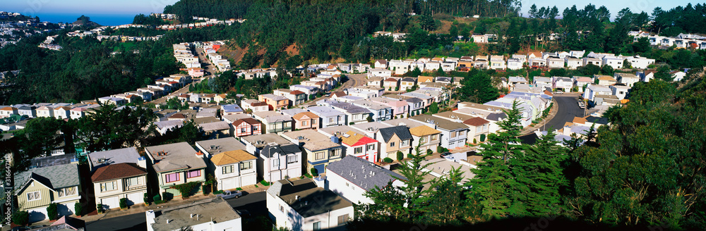 These are houses lined up in rows. They form a pattern and show urban congestion in housing. This is the view from Twin Peaks Mountain. There are green trees interspersed between the houses.