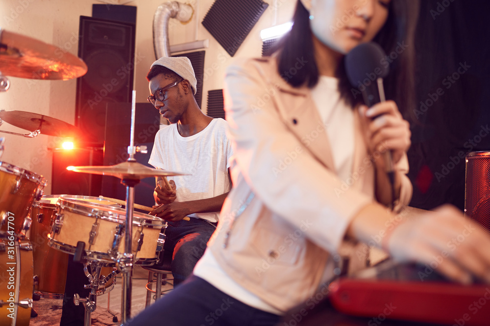 Portrait of contemporary band writing music in recording studio focus on young African man playing drums, copy space
