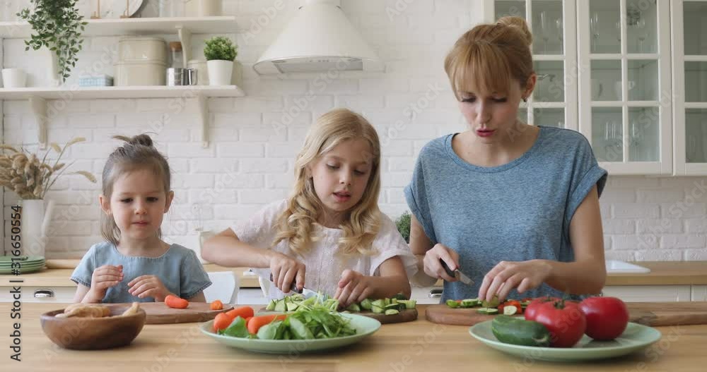 Cheerful young babysitter nanny talking to small sisters, teaching cooking.