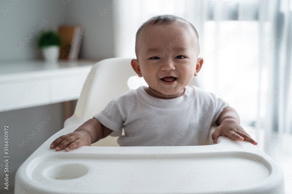 cute asian baby boy smiling to camera while eating sitting on high chair cute asian baby boy smiling to camera while eating sitting on high chair