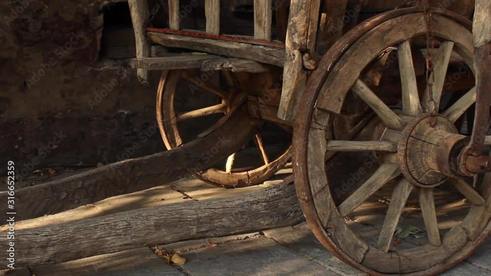Close up view of wooden cart wheels resting on pavement. slow pan right Close up view of wooden cart wheels resting on pavement. slow pan right