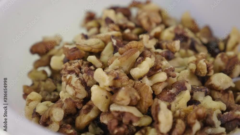 A white ceramic bowl full of peeled walnuts in close up. Daylight. Cooking ingredient. Nut snack. A white ceramic bowl full of peeled walnuts in close up. Daylight. Cooking ingredient. Nut snack.