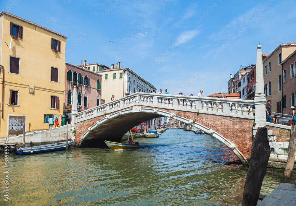 VENICE, ITALY - JUNE 15, 2016 View of the Ponte delle Guglie (Bridge of Spires) over the Canaregio Canal on a bright sunny day. A crowd of tourists on the bridge.