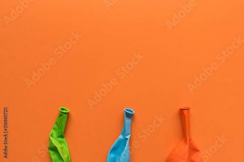 A few deflated multicolored balloons on an orange background.