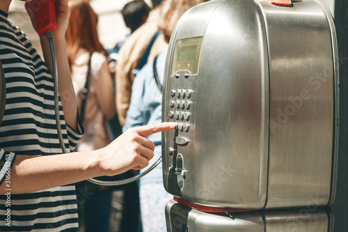 Fototapeta Naklejka Na Ścianę i Meble -  Close-up of a girl dialing a number or calling on a stationary street phone or from a telephone booth on a street in Italy.