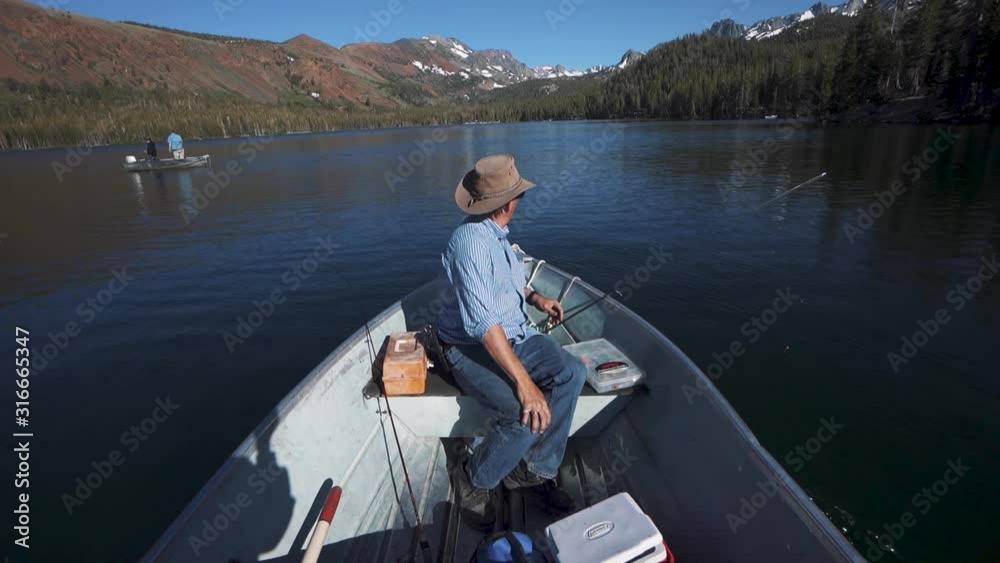 Older man fishing in a boat on a mountain lake Older man fishing in a boat on a mountain lake