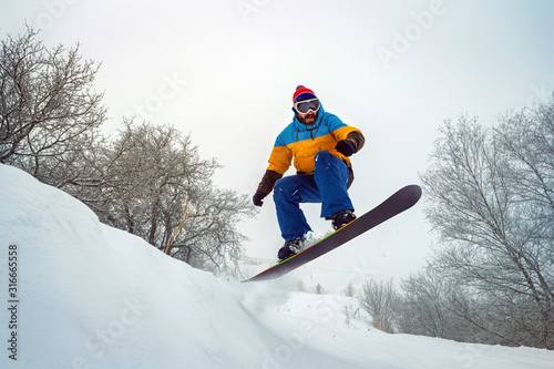 The guy is snowboarding. He jumps out of a snowy hill