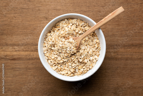 Oat flakes, oatmeal in bowl with wooden spoon on rustic wooden table background. Healthy eating, healthy food concept