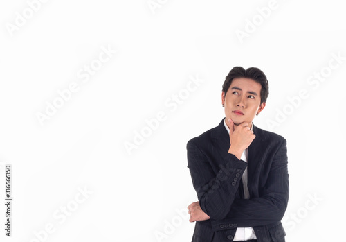 Portrait of an Asian business man wearing a black suit, standing with his arms crossed, hand on chin and looking up on a white background,isolated