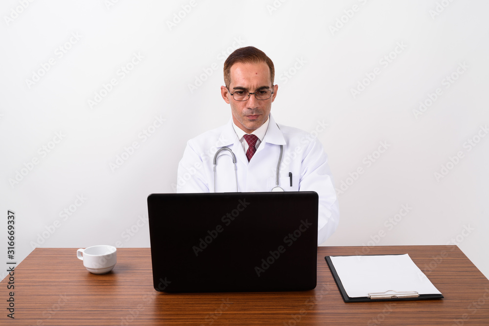 Mature Persian man doctor working behind desk Mature Persian man doctor working behind desk