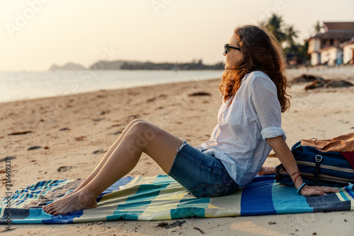 Young beautiful woman in sunglasses enjoying a summer day on the beach at sunset on a sandy beach by the sea