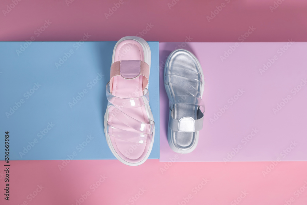 Fashionable gray and pink open slippers with a white sole and transparent straps stand on a pink, blue stand from the studio. Promotional photo Fashionable gray and pink open slippers with a white sole and transparent straps stand on a pink, blue stand from the studio. Promotional photo