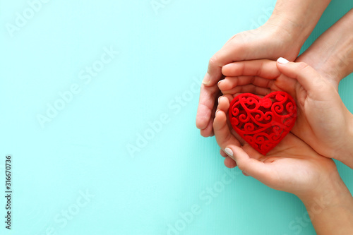 Valentine's, father's and mother's day background. Little child with mother heands holding red heart . Top view photo