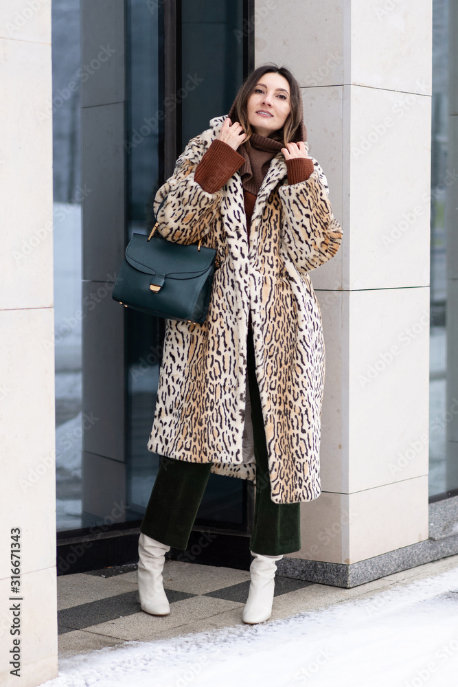 Fototapeta premium European girl in a leopard coat, corduroy pants with a handbag walks on the street. Life style