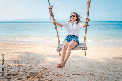 Beautiful young curly funny girl on a swing on a tropical beach,