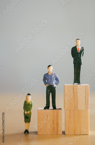 Gender equality concept, miniature female figurine stand lower than male figurines photo