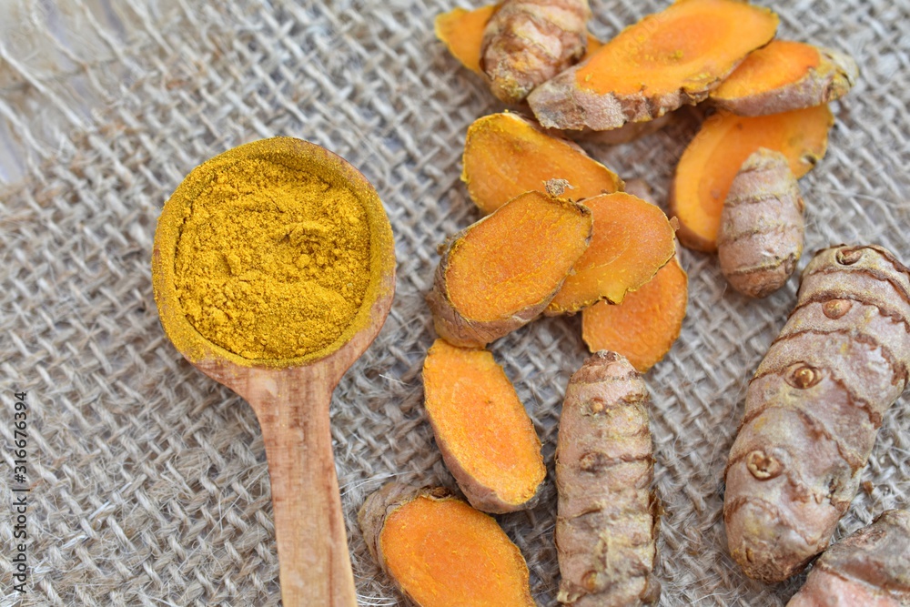 Turmeric roots and powder in wooden spoon, rustic background.