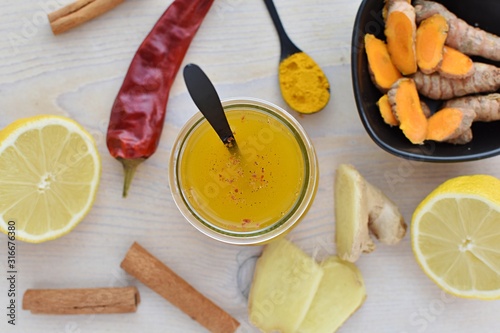 Hot, detox, spicy turmeric tea with chili peppers, lemon, ginger, cinnamon in small jar, top view.