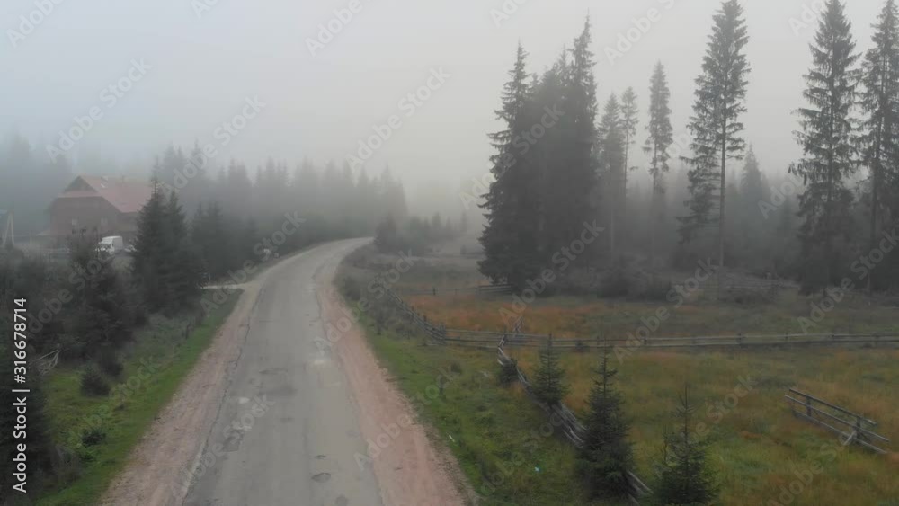 Foggy morning scene in mountain village. Road through forest in misty morning. Scenic rural view. Foggy morning scene in mountain village. Road through forest in misty morning. Scenic rural view.