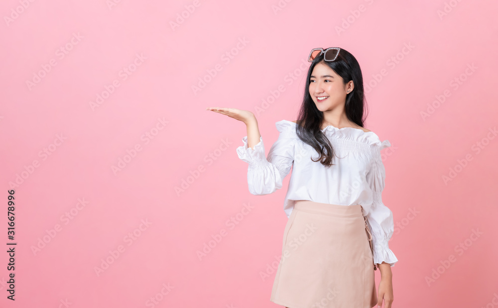 Young smiling Asian woman stand with open palms and looking to copy space on pink background. Young smiling Asian woman stand with open palms and looking to copy space on pink background.