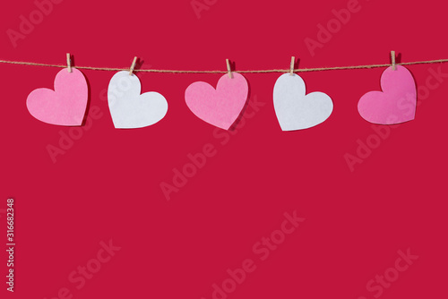 Garland of pink and white hearts on a red classic background. Natural rope and clothespins. Concept of Declaration of love, wedding, romantic relationship, Valentine's Day. Copy space