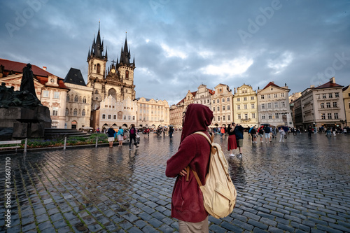 A man with a backpack and a red hoodie looks in surprise at the central square of the city of Prague. photo