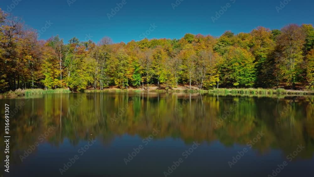 Aerial drone pan shot right to left of autumn forest trees near Lake Sevan in Armenia under bright blue sky. Colourful forest and water of Gosh Lake in armenian mountains in sunny day Aerial drone pan shot right to left of autumn forest trees near Lake Sevan in Armenia under bright blue sky. Colourful forest and water of Gosh Lake in armenian mountains in sunny day