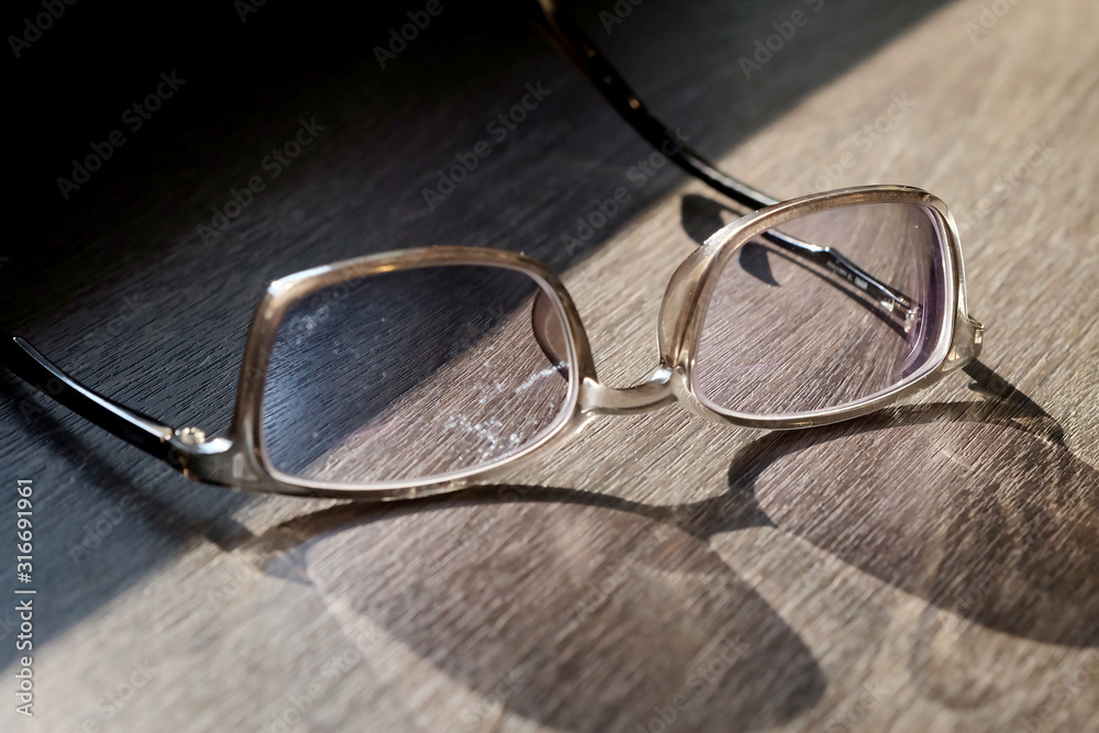 Old eye glasses on wood table in sunlight with shadow and space for write wording, dirty eye glasses may cause irritation and infection Old eye glasses on wood table in sunlight with shadow and space for write wording, dirty eye glasses may cause irritation and infection