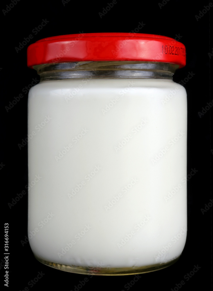 Small one hundred gram glass jar with white milk and a red lid isolated black macro Small one hundred gram glass jar with white milk and a red lid isolated black macro