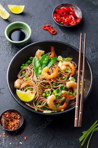 Stir fry noodles with vegetables and shrimps in black bowl. Dark slate background. Close up.