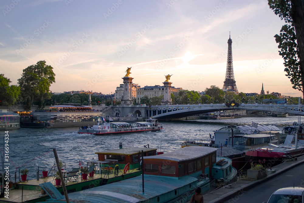 Beautiful sunset over the river Seine. Sailing pleasure boats with tourists, the Pont Alexandre III and the Eiffel Tower in the background.