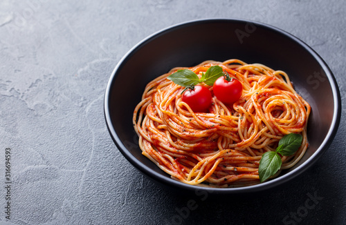 Pasta, spaghetti with tomato sauce in black bowl. Grey stone background. Close up. Copy space.