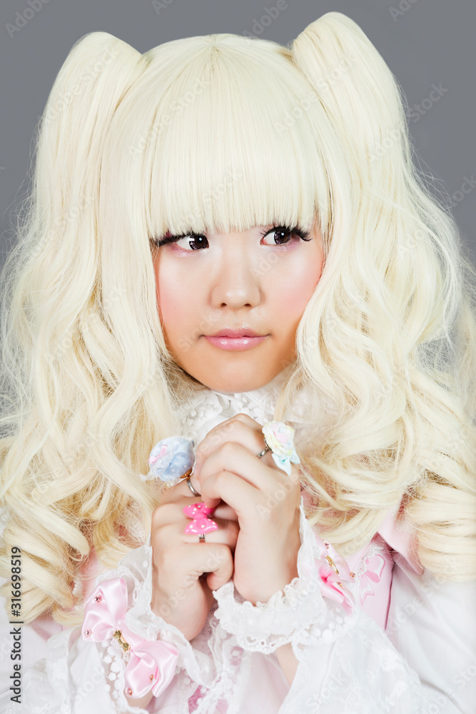 Cute young woman dressed as a doll over gray background