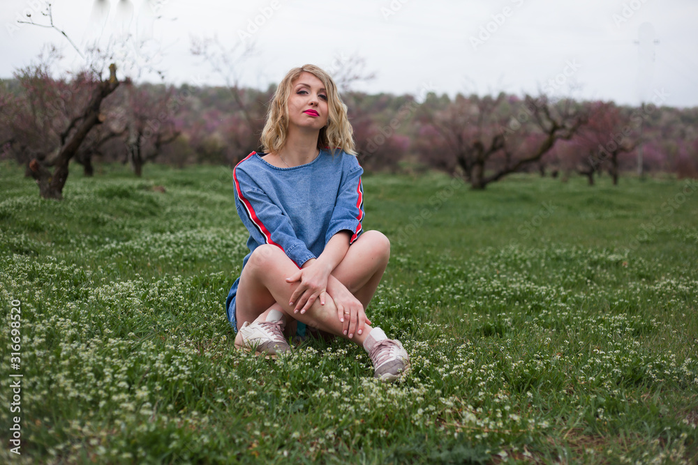 Fototapeta premium Unity with the nature of the woman, female sit on spring green grass in peach flower garden. It healthy to breath healthy air The model wearing denim dress .