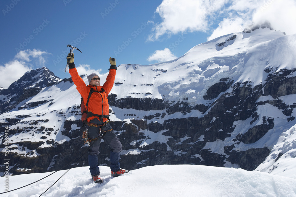 Mountain climber with arms raised on top of snowy peak