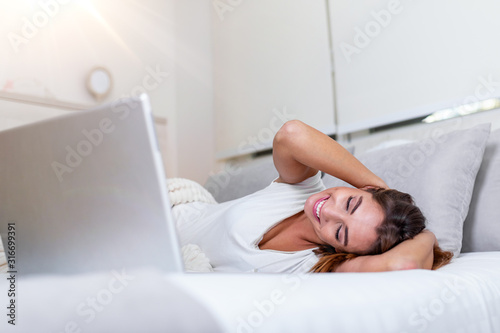 Attractive woman in white shirt using laptop and smiling at morning. Video chat and freelance working from home concept of beautiful young woman with laptop in bed