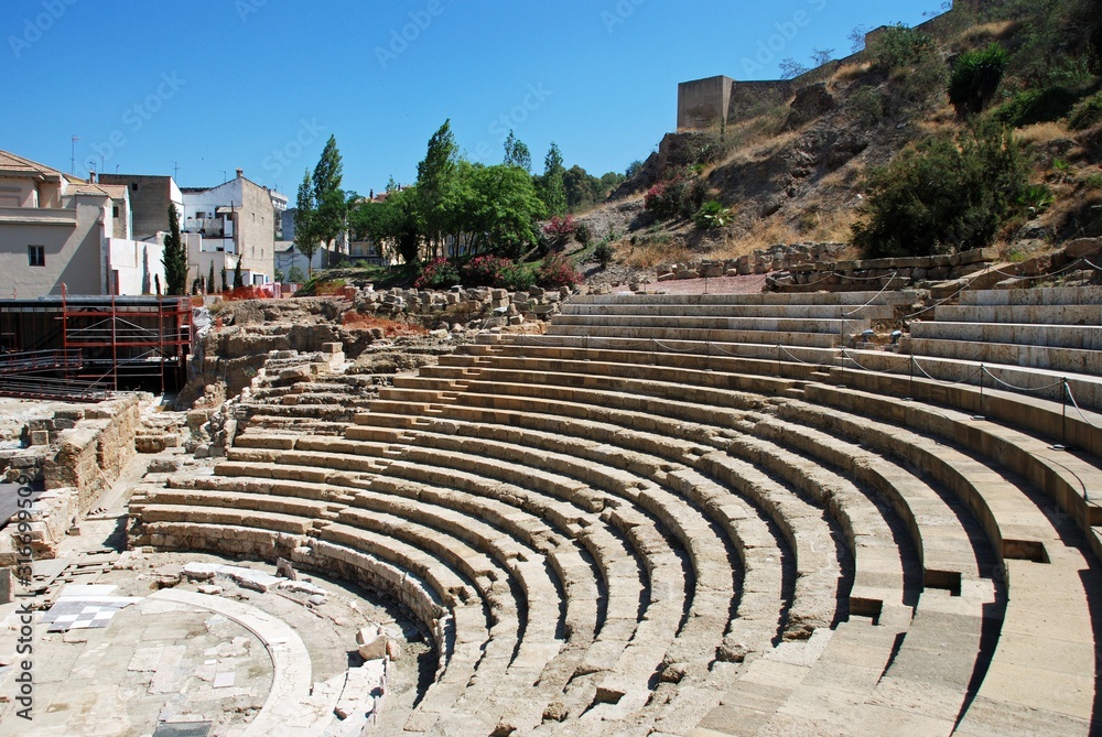 View of the Roman Amphitheatre in the city centre overlooked by the castle to the right, Malaga, Spain.