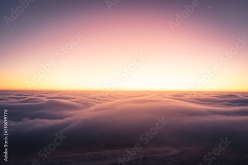 Winter landscape in Krkonose, beautiful sunrise with moon above the heavy clouds, shot from highest mountain in Czech republic called Snezka. © Tomas
