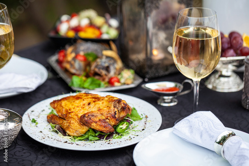 Baked full chicken with vegetables in a plate on a table next to glass of wine and candles. Outdoor  green park