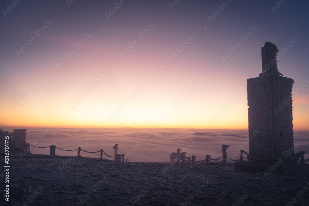 Winter landscape in Krkonose, beautiful sunrise with moon above the heavy clouds and some object that looks like bottle, shot from highest mountain in Czech republic called Snezka.