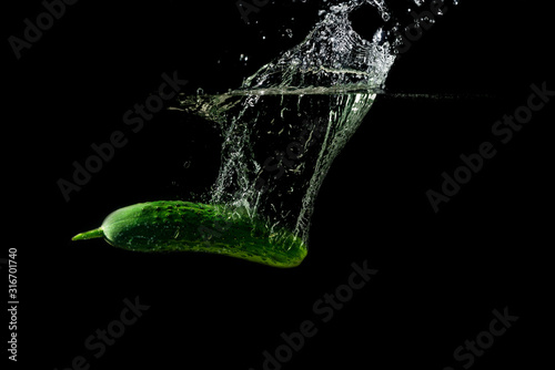Fresh green cucumber in water with splash on black background