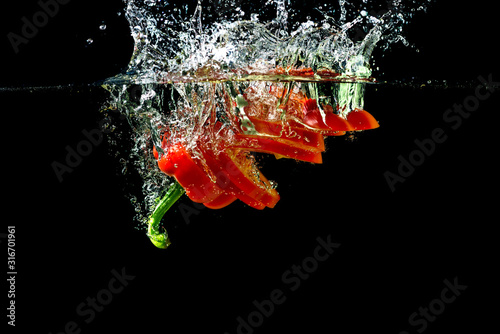 Red fresh paprika slices splash in water on a black background. Food concept.