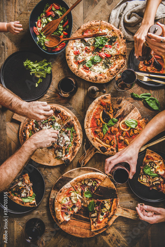 Family with baby having pizza party dinner. Flat-lay of people eating Italian pizza and drinking red wine from glasses over wooden table, top view. Fast food lunch, gathering, celebration