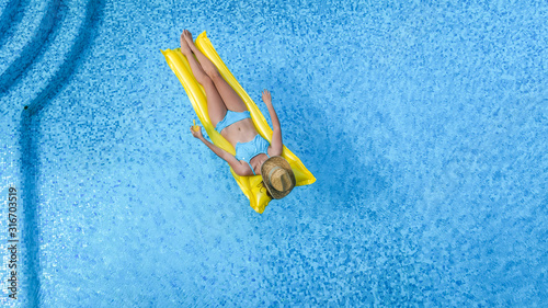 Beautiful young girl relaxing in swimming pool, swims on inflatable mattress and has fun in water on family vacation, tropical holiday resort, aerial drone view from above