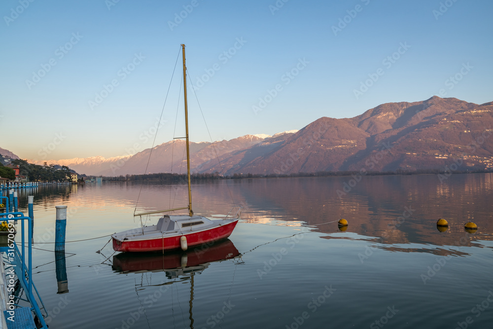 Colorful red boat on stunning mountain lake in Alps during sunset,panorama of Iseo lake from the city of Lovere,Bergamo,Lombardy Italy.