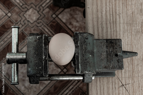 An egg cracking under pressure applied by squeezing clamps form the sides.
