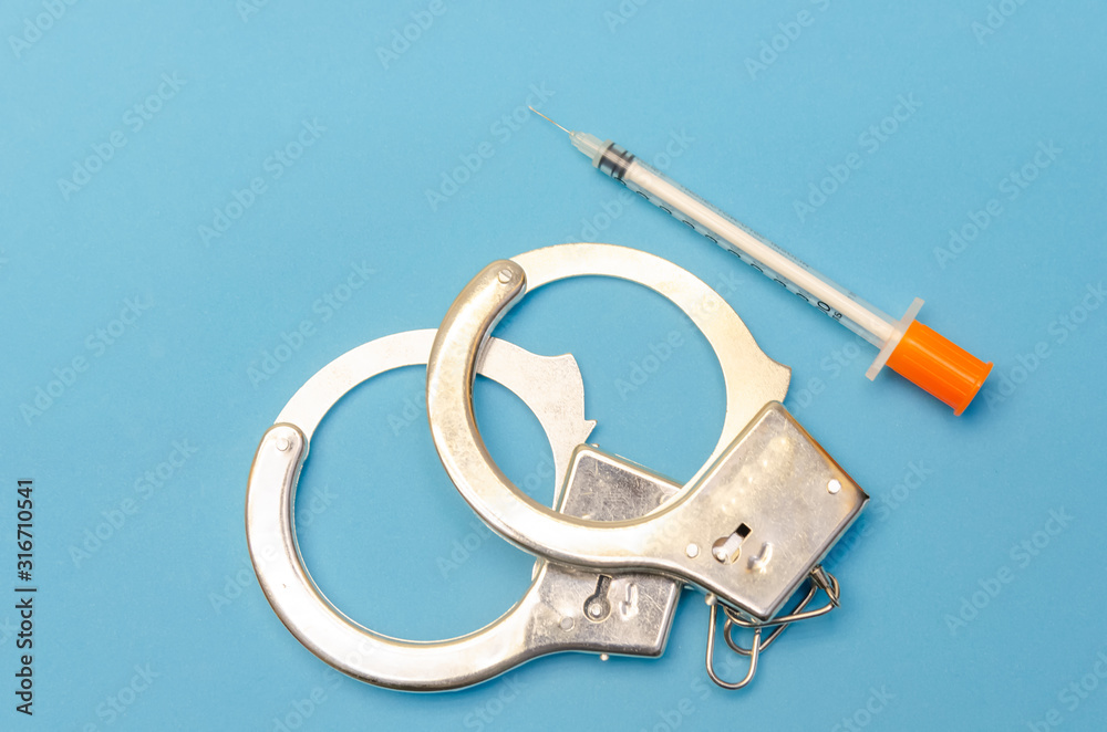 Handcuffs and a syringe on a blue background close-up Handcuffs and a syringe on a blue background close-up